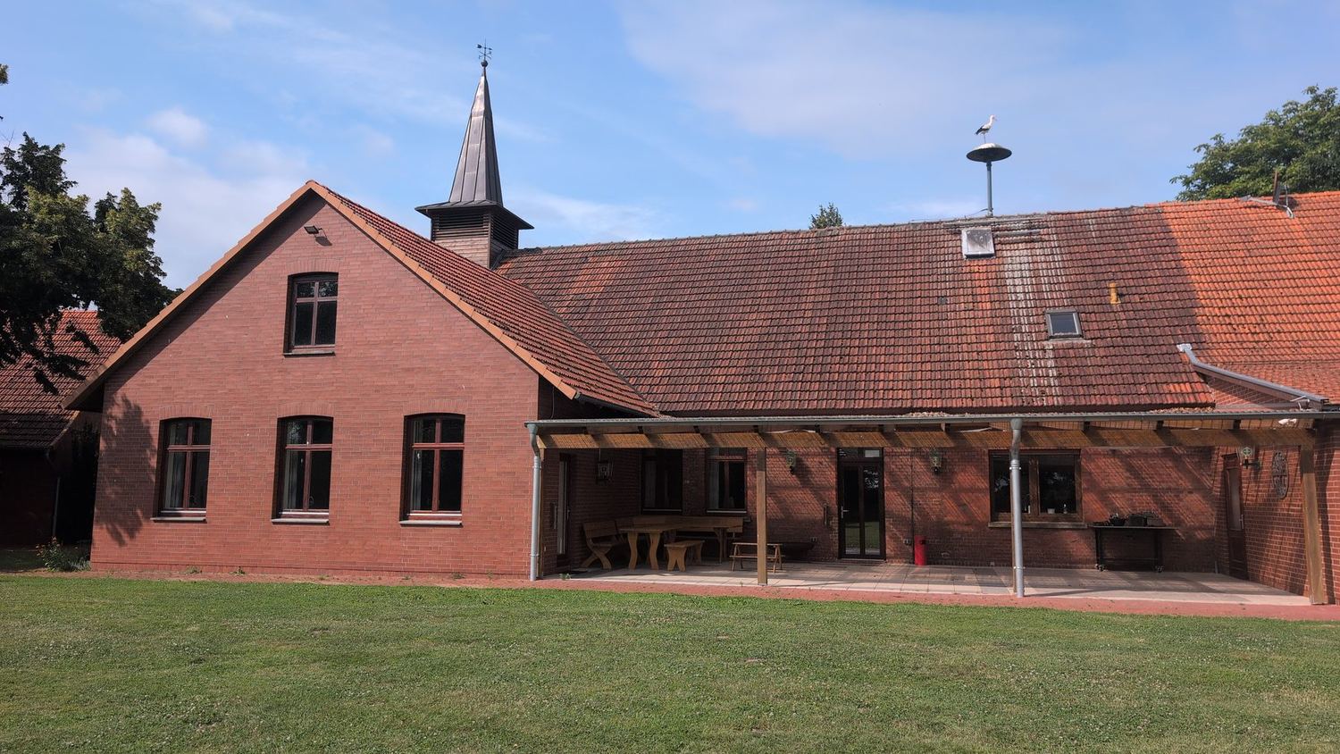 R&uuml;ckseite des Dorfgemeinschaftshauses mit &uuml;berdachter Terrasse und Sitzgelegenheiten